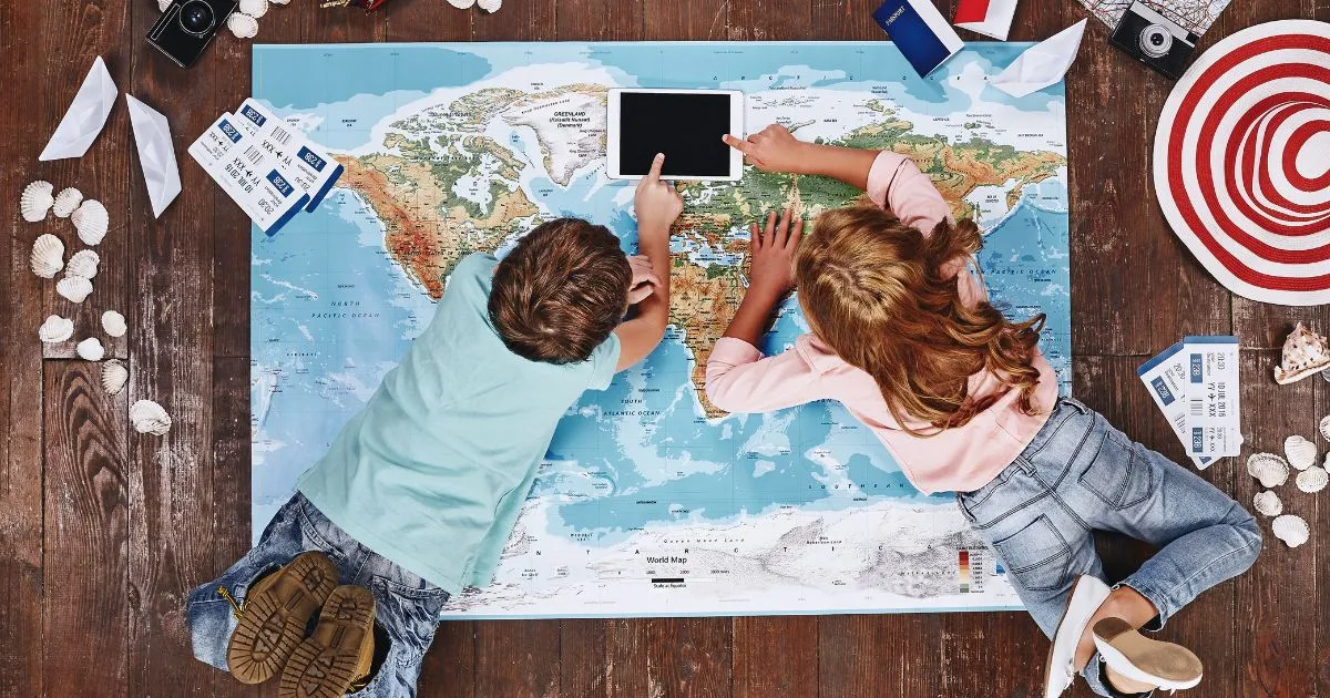 男の子と女の子が世界地図の上でタブレットを触っている